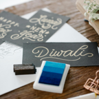 Handwritten calligraphy greeting cards for Diwali and New Year on a wooden table.